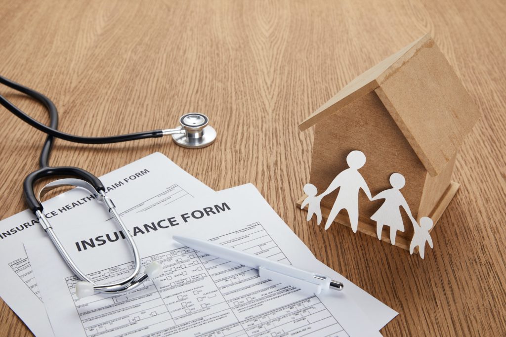 close-up view of insurance form, insurance health claim form, pen, stethoscope, house model and